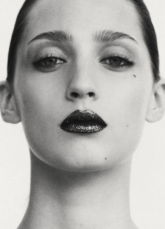 Close-up portrait of a woman with dark sparkly lipstick and dark eyeliner against a seamless white background.