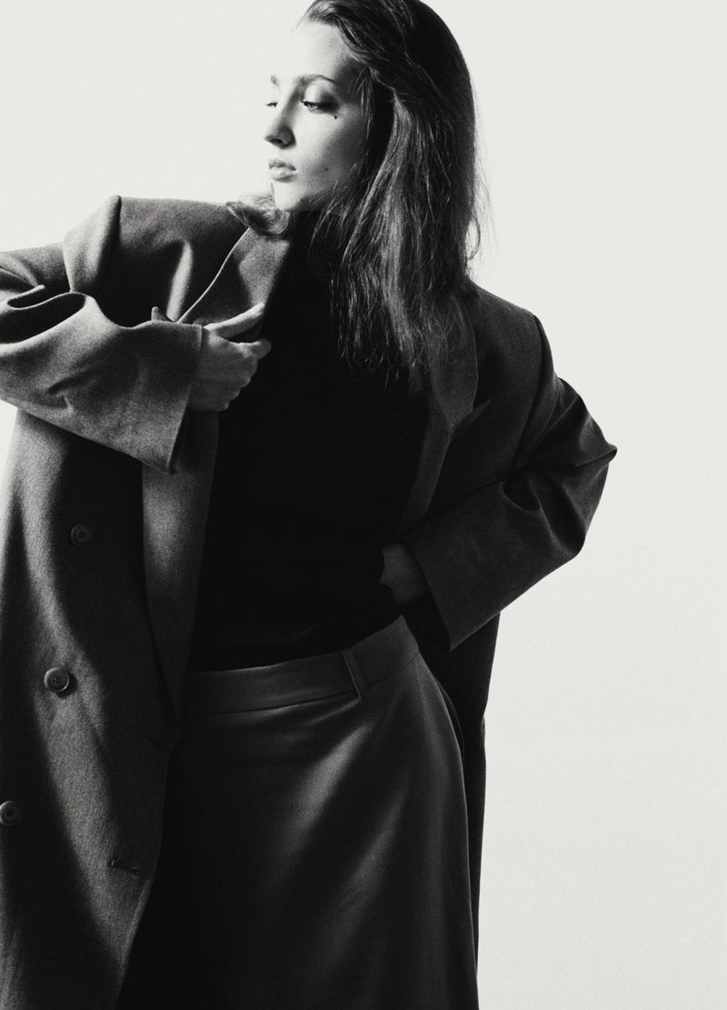 Model wearing a dark oversized blazer and matching skirt against a bright white studio background.