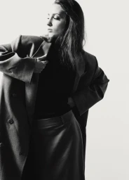 Model wearing a dark oversized blazer and matching skirt against a bright white studio background.