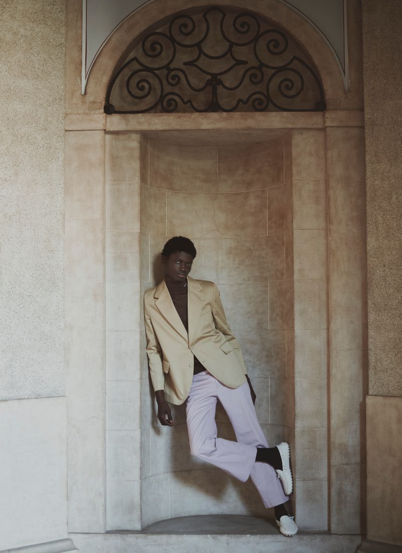 Model leaning inside a stone alcove wearing a tan blazer and light trousers for an ICON Magazine Mena editorial.