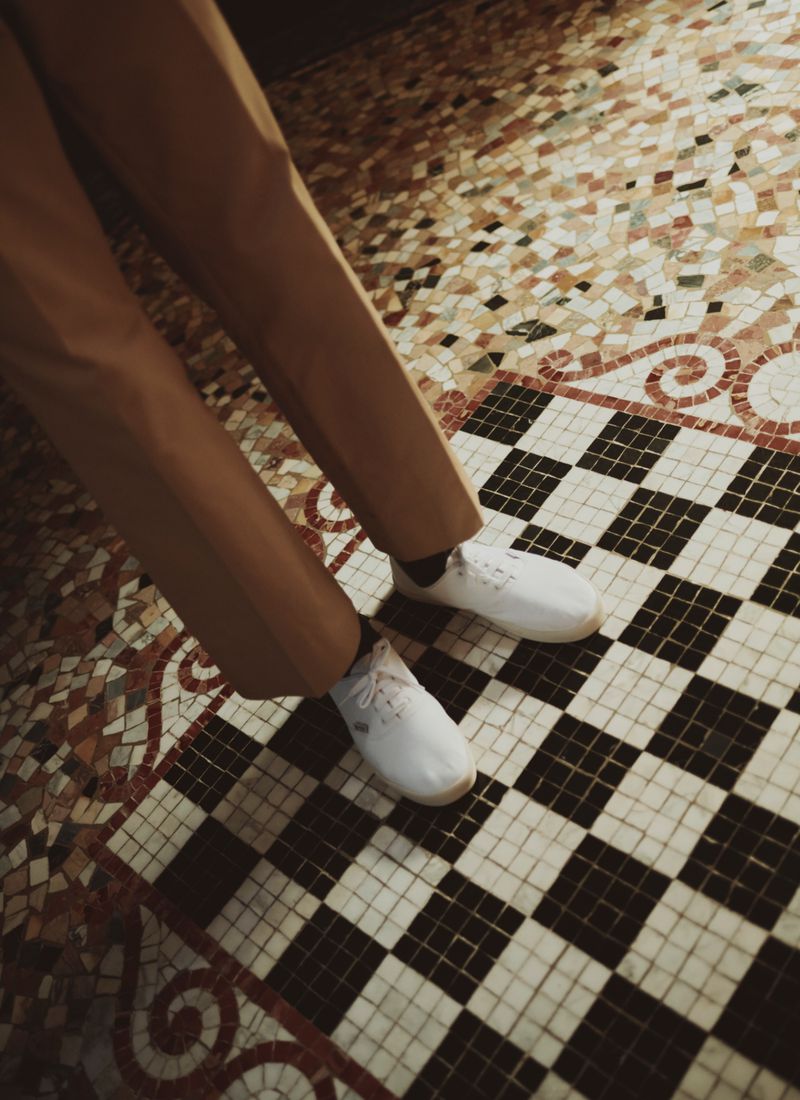 Close-up of trousers and white sneakers standing on a patterned mosaic tile floor