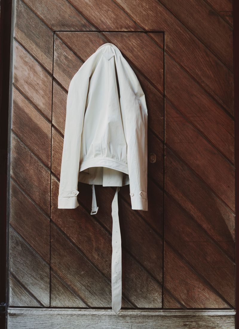 A cream-colored jacket hangs on a dark brown wood door with diagonal planks, creating a minimalist and neutral-toned composition.