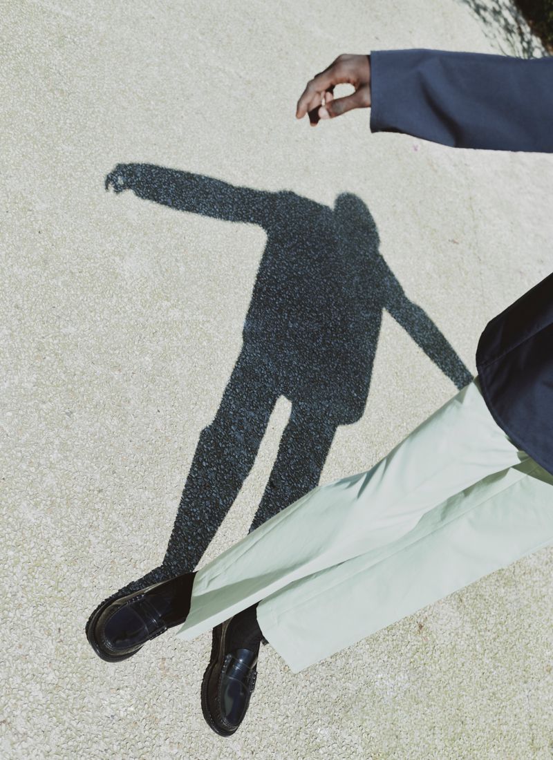Model wearing light green trousers and black loafers casting a shadow on a paved ground for Prada by ICON Magazine Mena