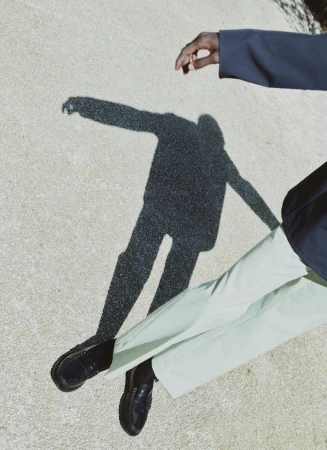 Model wearing light green trousers and black loafers casting a shadow on a paved ground for Prada by ICON Magazine Mena