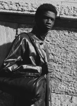 Model Seyi Adumati wearing Prada and carrying a leather bag against a stone wall in photography by Stefano Sciuto.