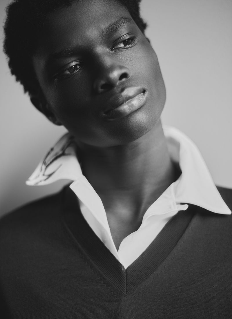 Monochrome portrait of a black man wearing a collared shirt and v-neck sweater against a plain background