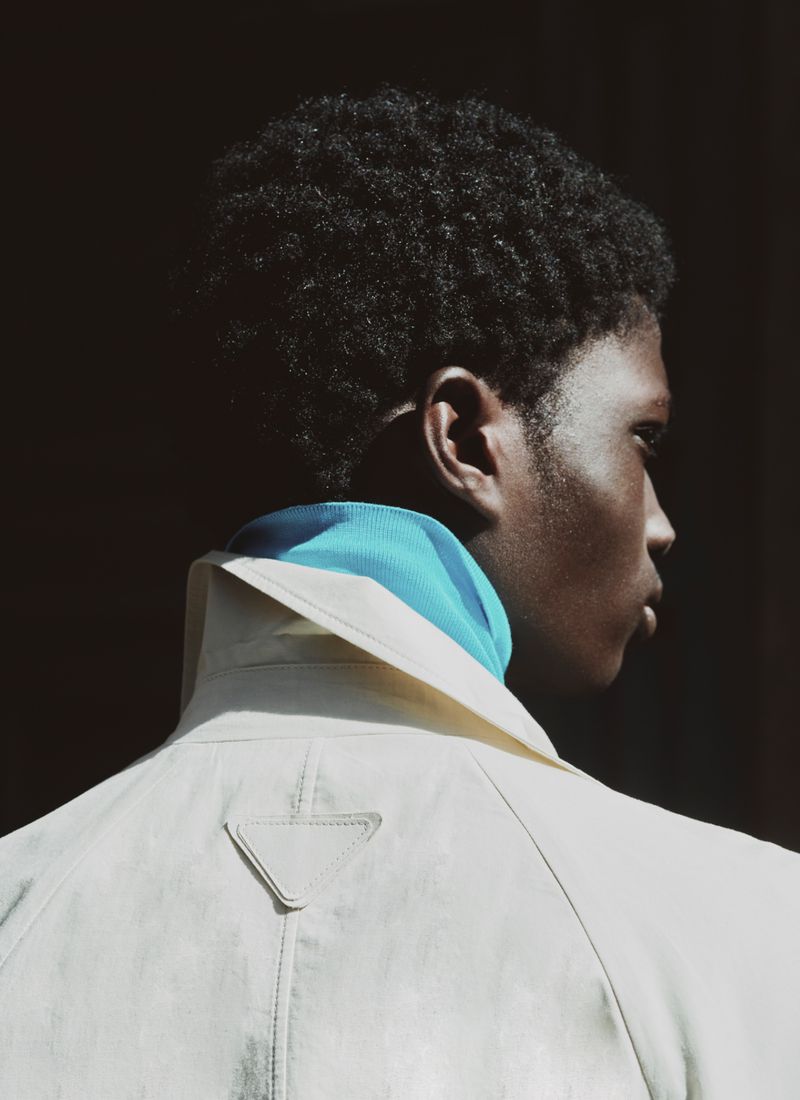 Close-up profile of a black man wearing a light beige coat and blue turtleneck collar