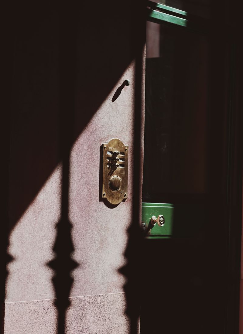 Close-up of an ornate brass doorbell panel mounted on a textured exterior wall with dramatic shadows.