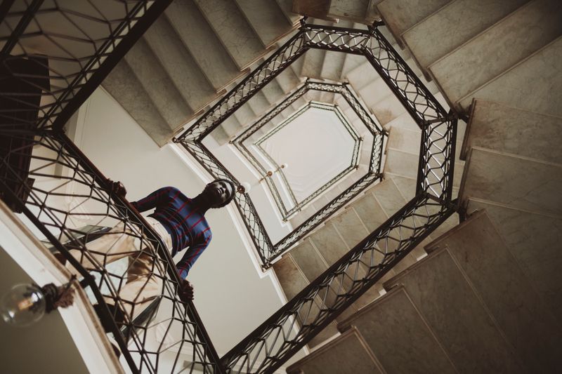 Low-angle view of a man standing on an ornate winding staircase inside a building for an editorial shoot.