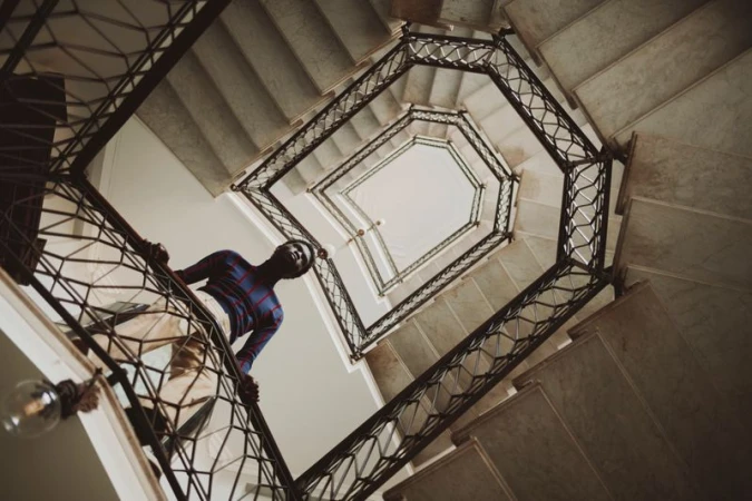 Low-angle view of a man standing on an ornate winding staircase inside a building for an editorial shoot.