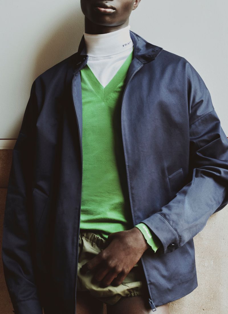 Model wearing a dark blue jacket over a green v-neck sweater and white turtleneck for Prada in ICON Magazine Mena