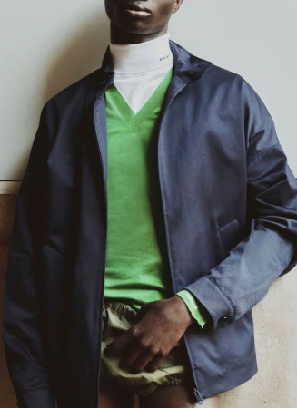 Model wearing a dark blue jacket over a green v-neck sweater and white turtleneck for Prada in ICON Magazine Mena