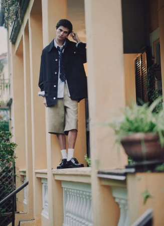 Young male model in dark jacket and tie standing on a yellow building veranda for an ICON Magazine Mena editorial