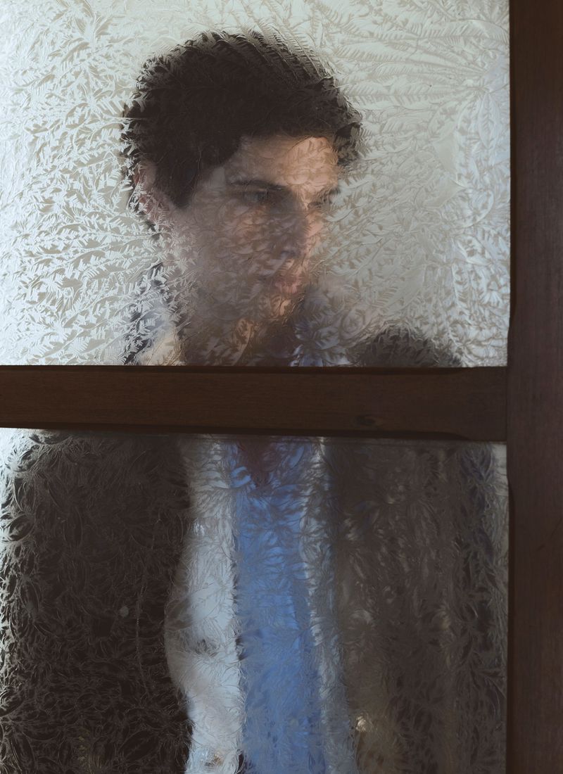 Man behind patterned frosted glass pane wearing dark jacket and blue shirt