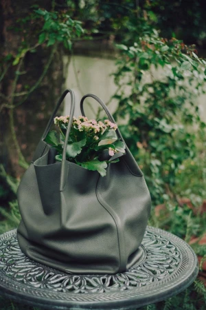 Grey leather tote bag filled with small pink flowers sitting on a decorative metal table outdoors