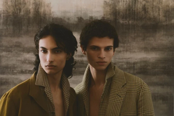 Two male models posing against a dark muted painted landscape backdrop for an ICON Magazine Mena fashion editorial project titled Idle Times.