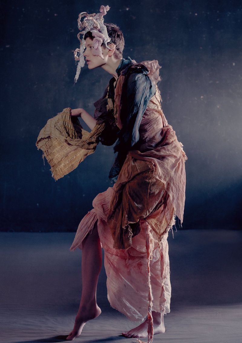 Model Saskia de Brauw in avant-garde draped attire holding a textured fabric against a dark textured background for Luncheon Magazine.