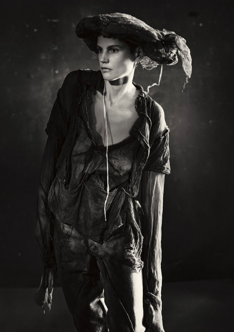 Model Saskia de Brauw in dark draped clothing and wide hat against dark background for Luncheon Magazine