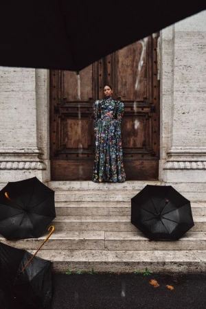 Model wearing floral dress standing on stone steps framed by black umbrellas