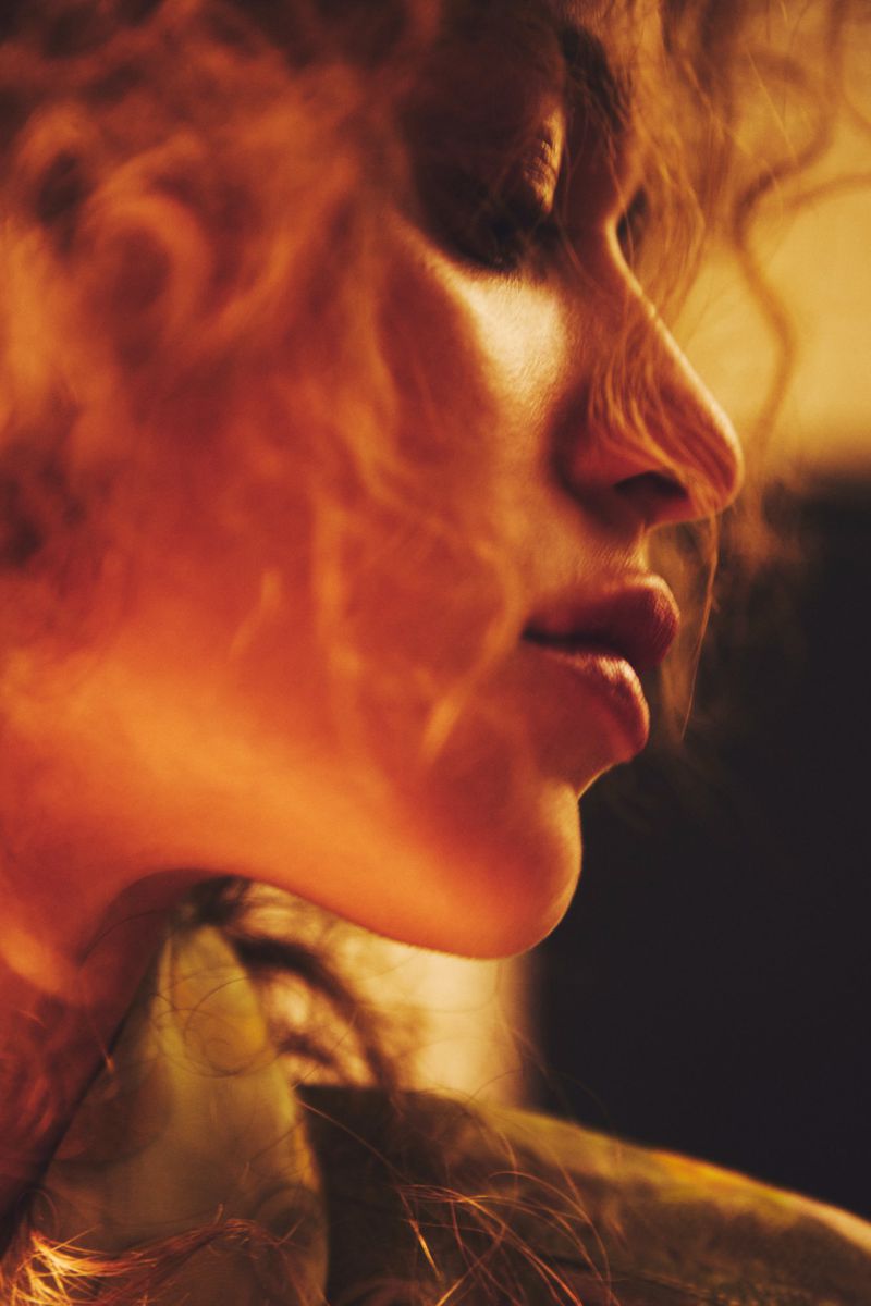 Close-up profile portrait of a woman with curly hair under warm golden lighting for Elle Slovenia