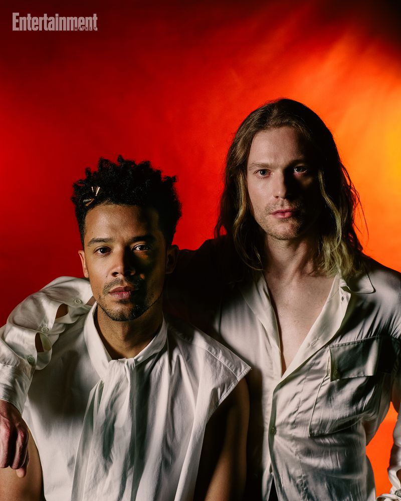 Two men in white shirts posing against a vibrant red and orange studio backdrop for Entertainment Weekly.