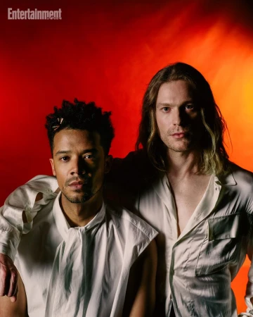 Two men in white shirts posing against a vibrant red and orange studio backdrop for Entertainment Weekly.