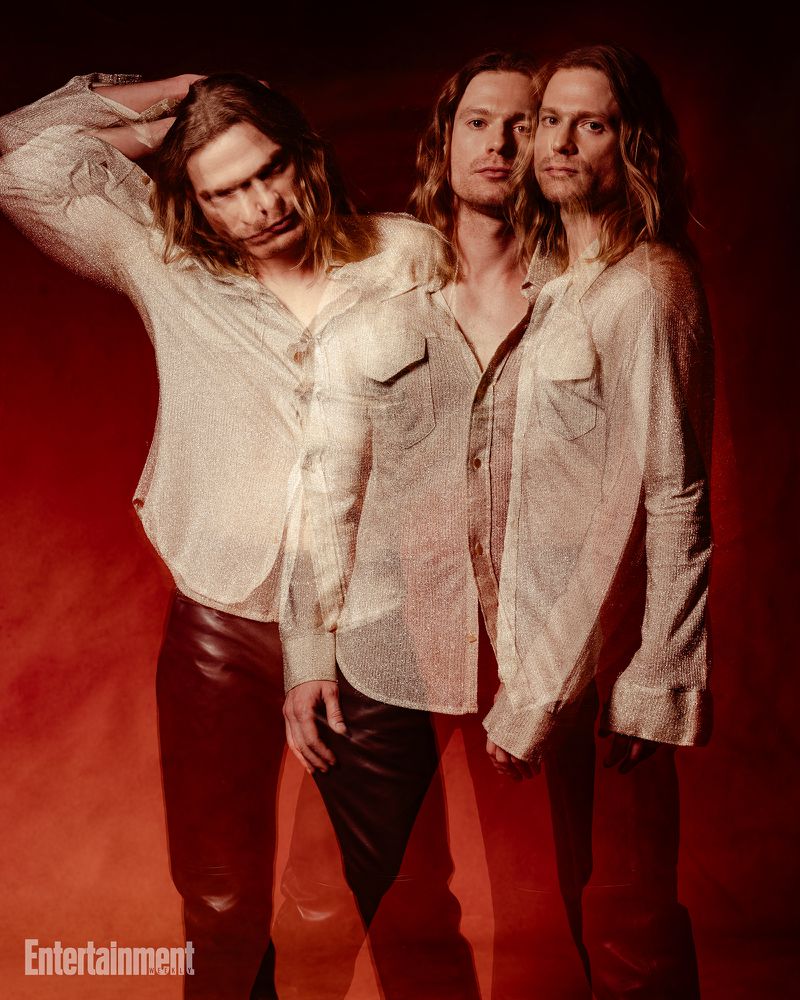 Multiple exposure portrait of a man with long hair wearing a patterned shirt and dark trousers against a red background
