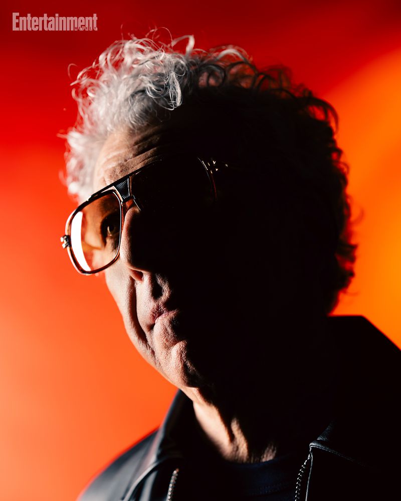 Portrait of a man wearing tinted sunglasses and a dark jacket against a vibrant red and orange background for Entertainment Weekly.