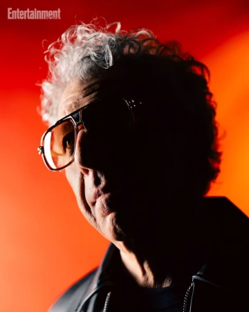 Portrait of a man wearing tinted sunglasses and a dark jacket against a vibrant red and orange background for Entertainment Weekly.
