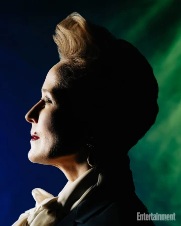 Profile portrait of a white woman with updo hair and dark blazer against a blue and green lit background for Entertainment Weekly.