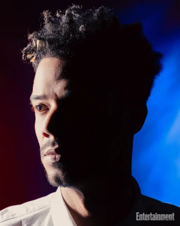 Portrait of a Black man with short dark hair in profile, lit by dramatic red and blue studio lighting for Entertainment Weekly.