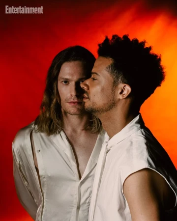 Two men in white shirts posing closely together against a vibrant red and orange gradient background for Entertainment Weekly.