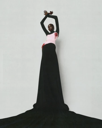 Model in a black long-sleeve top and pink corset with black floor-length skirt against a grey studio backdrop.