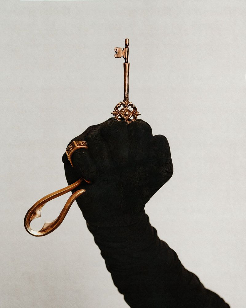 Gloved hand holding a golden antique key against a neutral background for Swallow The Key editorial by Glamcult Magazine