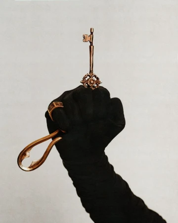 Gloved hand holding a golden antique key against a neutral background for Swallow The Key editorial by Glamcult Magazine