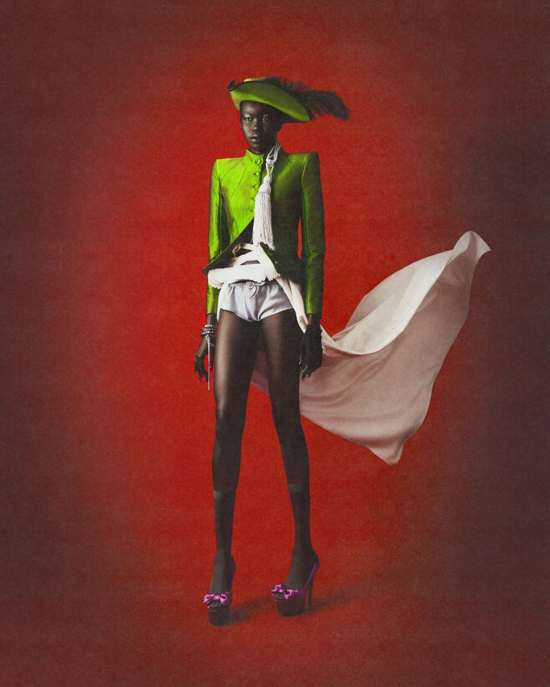 Black woman wearing a green jacket, matching hat with feather, and white flowing skirt against a red textured background