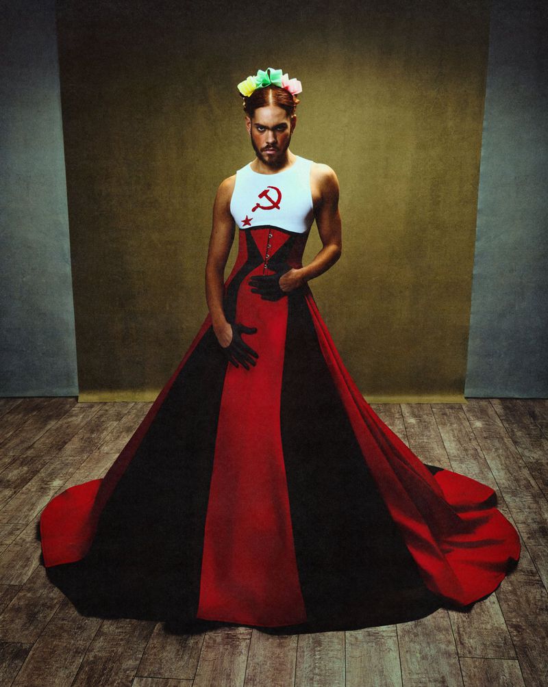 Man wearing a long red, black and white gown with a hammer and sickle emblem, photographed by Gustavo Chams.