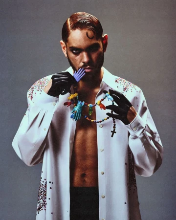 Man wearing a white shirt and black gloves holding a colourful toy hand necklace against a grey studio background