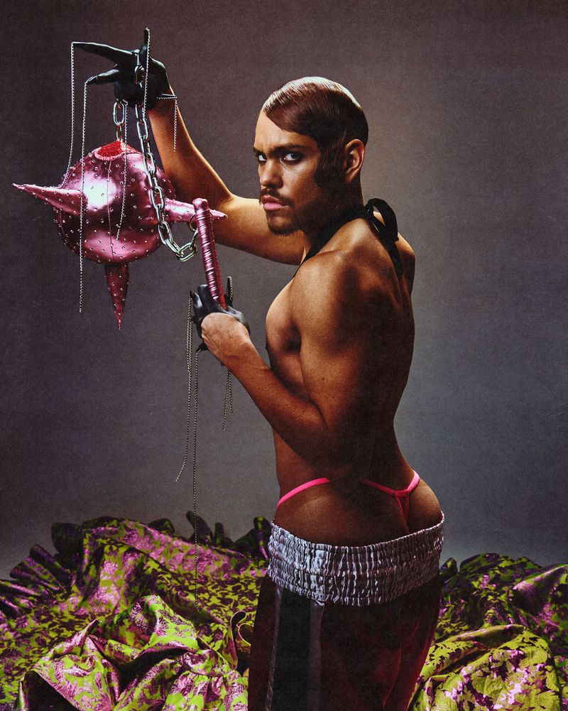 Man holding a spiked pink mace sculpture wearing shorts and a pink thong in an editorial portrait by Gustavo Chams for Fault Magazine.