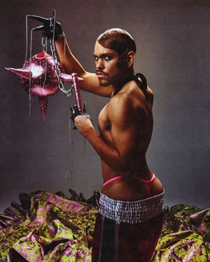 Man holding a spiked pink mace sculpture wearing shorts and a pink thong in an editorial portrait by Gustavo Chams for Fault Magazine.