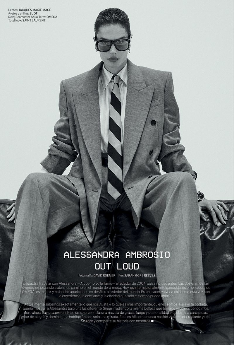 Alessandra Ambrosio in oversized gray suit and striped tie poses on a black leather couch in black and white fashion editorial.