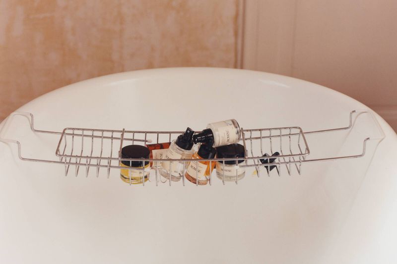 Several skincare bottles arranged in a metal caddy resting across a white porcelain bathtub.