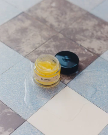 Rowse skincare glass jar with yellow balm and black cap resting on patterned tiled surface