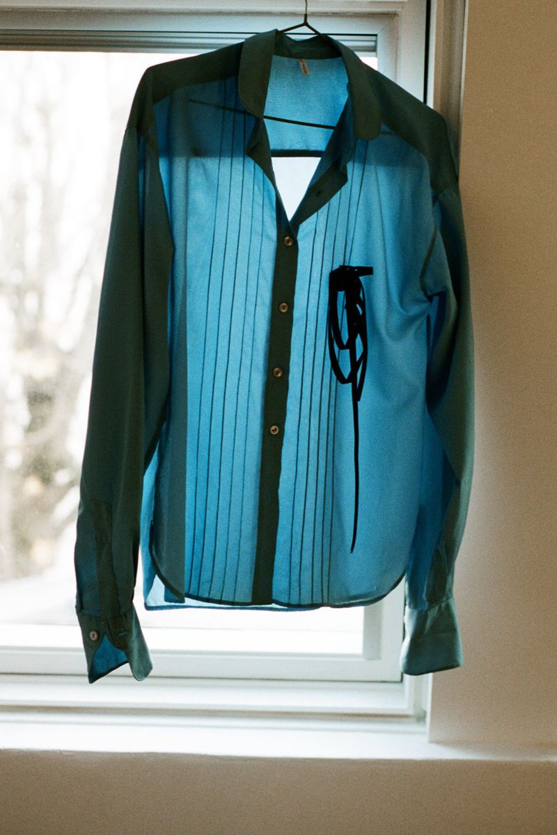 Blue and green button-down shirt hanging on a wire hanger in front of a bright window
