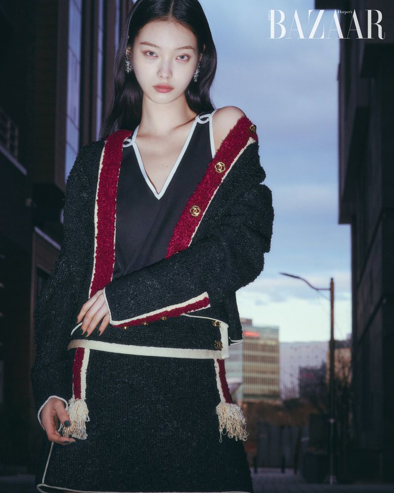 Model wearing a black tweed jacket with red trim standing on a city street at dusk for Harper's Bazaar Korea.