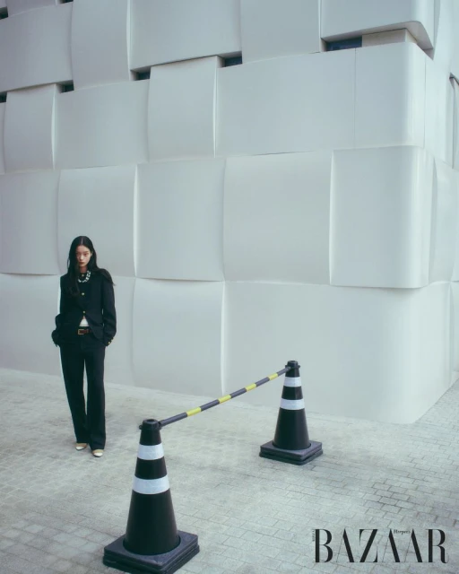 Model wearing dark suit standing near traffic cones and a modern white building facade