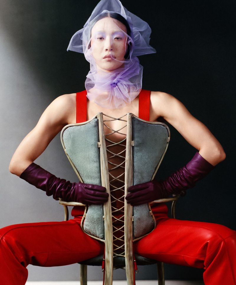 Model Sora Choi in a sculptural laced corset, red trousers, and purple tulle headdress for T Magazine by Luis Alberto Rodriguez.