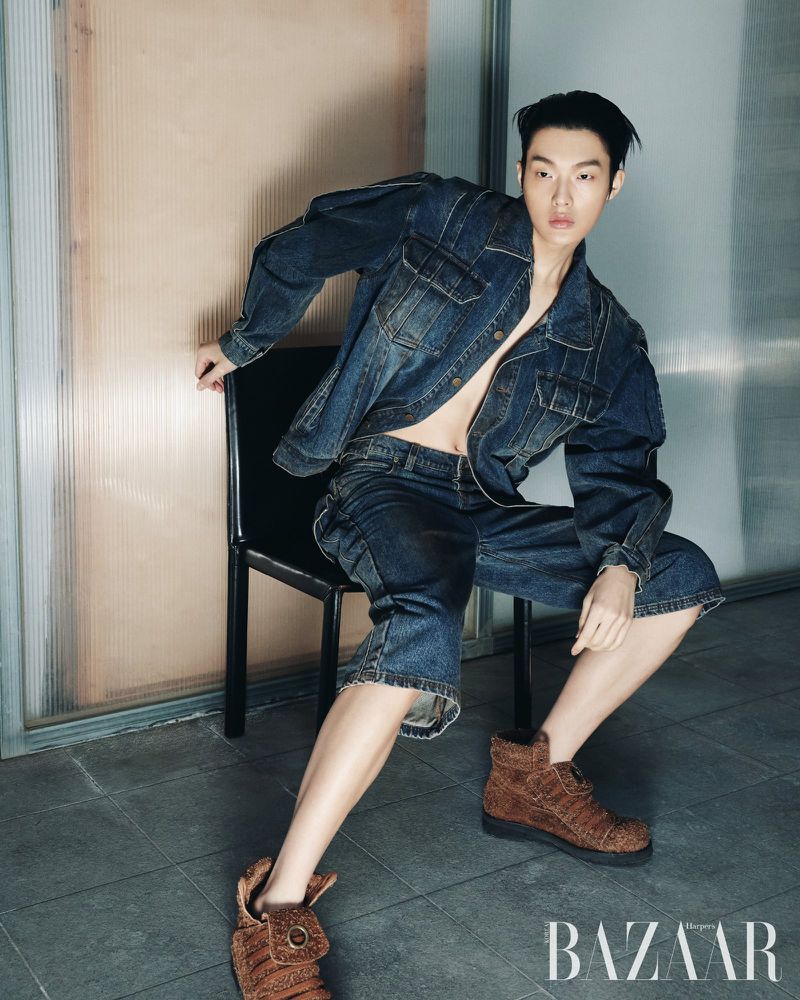 Model seated on a black chair wearing a denim jacket and jeans with brown boots for Harper's Bazaar Korea