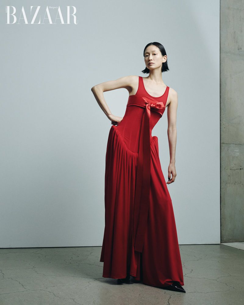 Model in a red dress with a bow detail standing against a neutral studio backdrop for Harper's Bazaar Korea