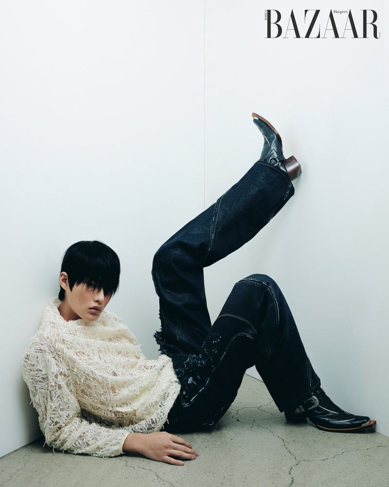 Model with dark hair wearing a textured cream sweater and dark pants against a white wall.